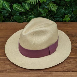 May include: A light beige Panama hat with a wide brim and a purple ribbon band.