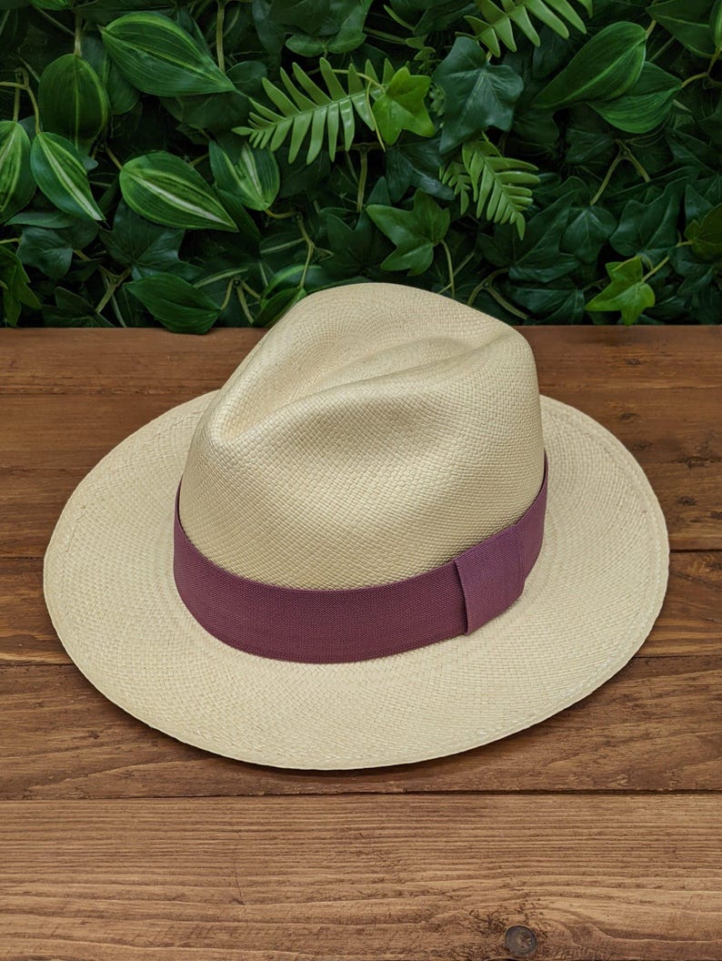 May include: A light beige Panama hat with a wide brim and a purple ribbon band.