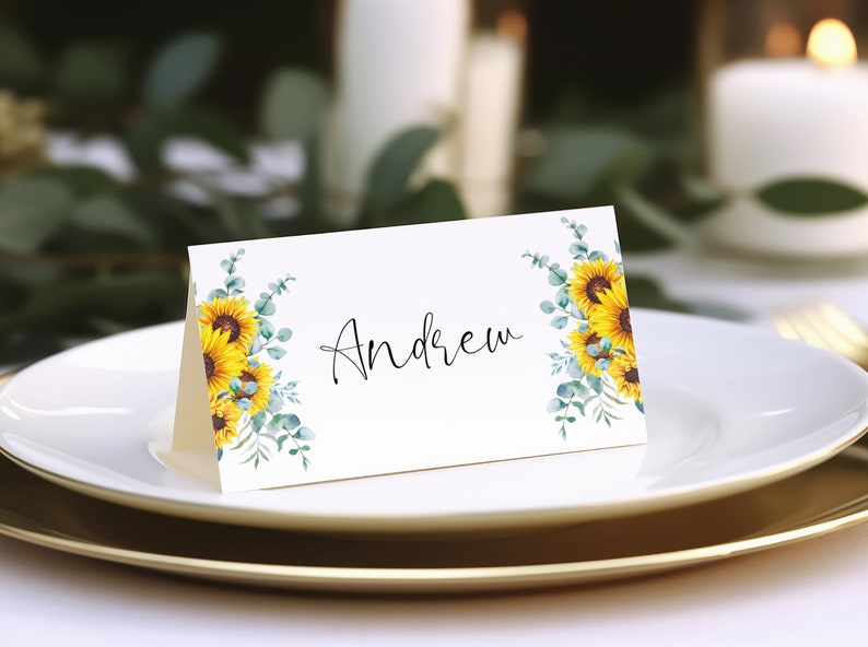 Puede incluir: Una tarjeta de lugar blanca con un dise&ntilde;o de girasol y eucalipto. El nombre "Andrew" est&aacute; escrito en cursiva negra.