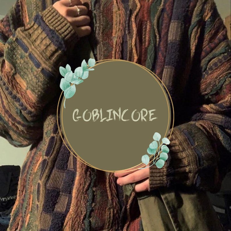 May include: A multi-colored knitted sweater with a brown, green, and blue color scheme. The sweater has a cable knit pattern and a relaxed fit. The text "GOBLINCORE" is written in a circle on the sweater.