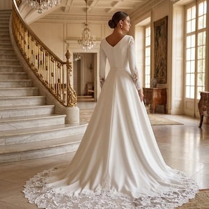 Peut inclure: Robe de mariée blanche à manches longues et col en V. La robe présente une longue traîne avec un ourlet en dentelle. Les manches ont des détails en dentelle aux poignets. La scène se déroule dans un grand hall avec un escalier en marbre et des lustres.