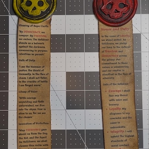 May include: Two decorative bookmarks with skull emblems. One is yellow with text about democracy and duty. The other is red with text about liberty and honor. Both have a distressed, vintage appearance.