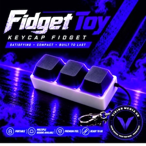 Könnte beinhalten: Ein rechteckiges weißes Fidget-Spielzeug mit drei schwarzen mechanischen Tastaturkappen auf der Oberseite. Das Gerät verfügt über einen Metallschlüsselanhänger und wird vor einem dunklen Hintergrund mit blauer Beleuchtung und dem Text Fidget Toy gezeigt.