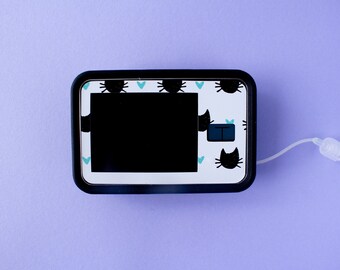 May include: A black and white medical device with a cat design. The device has a small screen and a white tube attached to it.