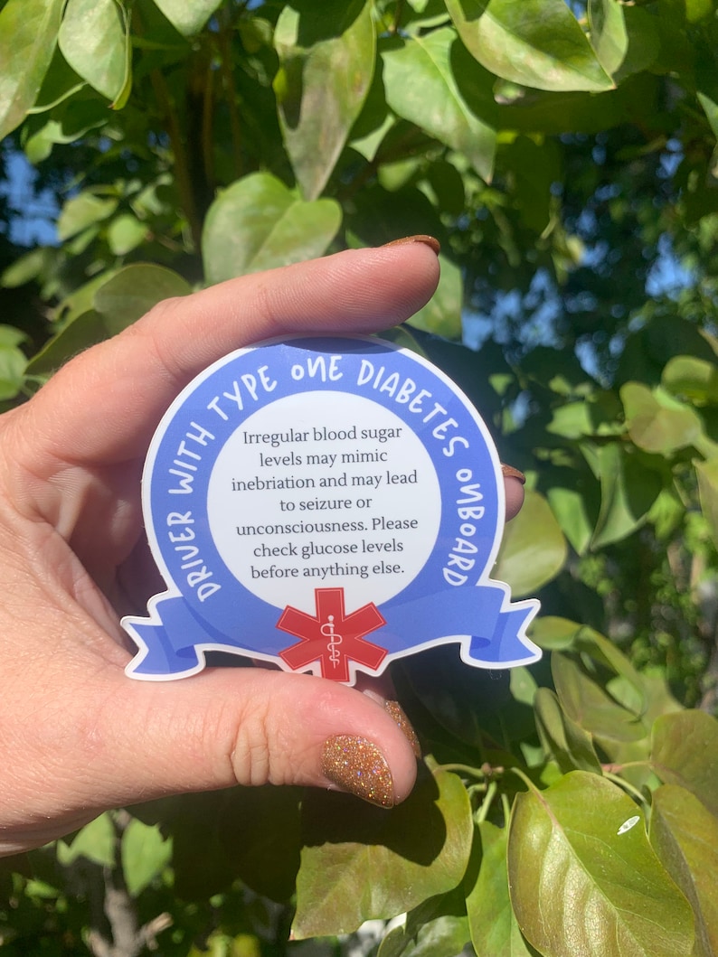 May include: Blue and white sticker with the text "DRIVER WITH TYPE ONE DIABETES ONBOARD". The sticker has a red medical symbol with a snake wrapped around a staff. The text reads: "Irregular blood sugar levels may mimic inebriation and may lead to seizure or unconsciousness. Please check glucose levels before anything else."