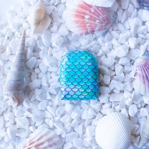 Könnte beinhalten: Ein blaues und grünes Nagellackdesign mit Meerjungfrauen-Schuppen auf weißem Hintergrund mit Muscheln.