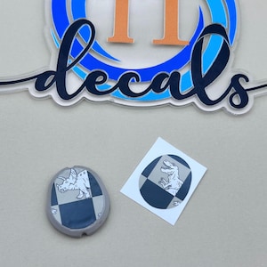 May include: Two round stickers with a black and white checkered background. One sticker features a white outline of a triceratops dinosaur. The other sticker features a white outline of a T-Rex dinosaur.