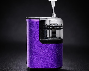 May include: A purple glitter-covered device with a clear, cylindrical top and a white, rectangular cap. The device has a black base and a clear, cylindrical component with measurements. The background is black.
