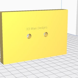 Op de afbeelding: Een geel rechthoekig object met twee cirkelvormige gaten. De tekst "3D Man Designs" is op het oppervlak gedrukt. Het object staat schuin, waardoor de dikte zichtbaar is.