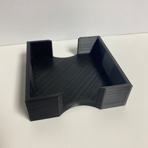 May include: A black, rectangular desk organizer with a curved cutout on one side. The organizer is made of a textured material and has a simple, modern design. The organizer is designed to hold small items.