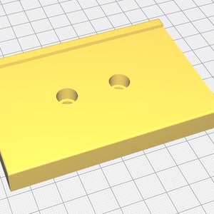 Op de afbeelding: Een effen geel rechthoekig object met twee cirkelvormige gaten. De bovenkant heeft een verhoogde rand langs &eacute;&eacute;n kant. Het object staat tegen een rasterachtergrond, wat wijst op een 3D-model of ontwerpelement.