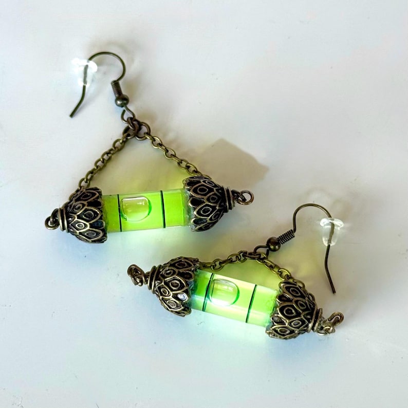 May include: A pair of green level earrings with antique gold-toned metal accents. The earrings are suspended from a chain and have a hook closure.