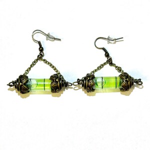 May include: A pair of gold-toned earrings with a green level bubble in the center. The earrings are suspended from a chain and have a decorative design on the ends.