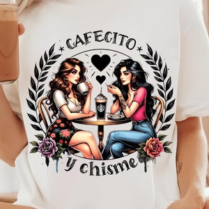 Puede incluir: Camiseta blanca con un gráfico de dos mujeres en una mesa con café, rodeadas por una corona floral. El texto "Cafecito y chisme" está arriba y abajo de la imagen. Las mujeres tienen cabello oscuro y visten ropa informal.