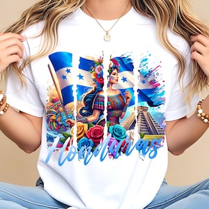 Puede incluir: Camiseta blanca con un diseño gráfico colorido. El diseño incluye la palabra "Honduras" en azul, la bandera hondureña, una mujer con vestimenta tradicional, flores y una pirámide.