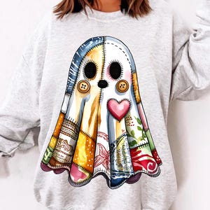 Pode incluir: Um moletom cinza claro com um design de fantasma de patchwork colorido. O fantasma tem olhos de botão, um coração rosa e um contorno costurado. O patchwork inclui vários padrões e cores.