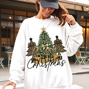Pode incluir: Camisola branca com um design de Natal. O design apresenta uma árvore de Natal decorada, árvores com estampa de leopardo, presentes embrulhados e a frase "Merry Christmas". Uma estrela dourada coroa a árvore.