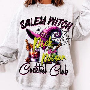 May include: A light gray sweatshirt with a graphic design featuring a witch's hat, cocktails, and the text "Salem Witch Cocktail Club." The design includes a spider, a spiderweb, and the words "Pick Your Poison."