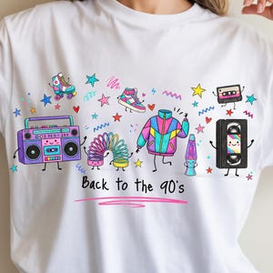 May include: A white t-shirt featuring a colorful graphic print of 1990s themed items including a boombox, roller skate, slinky, windbreaker, lava lamp, cassette tape, and VHS tape with the text Back to the 90's written in black script.