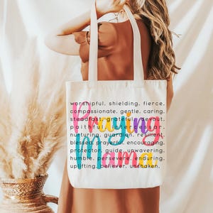Peut inclure: Un sac fourre-tout en toile blanche avec le mot "Prier" en lettres color&eacute;es et une liste de mots d&eacute;crivant les qualit&eacute;s d'une personne qui prie. Les mots incluent : respectueux, protecteur, f&eacute;roce, compatissant, doux, attentionn&eacute;, ferme, reconnaissant, d&eacute;vou&eacute;, fid&egrave;le, intercesseur, nourricier, gardien, r&eacute;silient, b&eacute;ni, fervent, encourageant, protecteur, guide, in&eacute;branlable, humble, pers&eacute;v&eacute;rant, durable, &eacute;difiant, croyant, in&eacute;branlable.