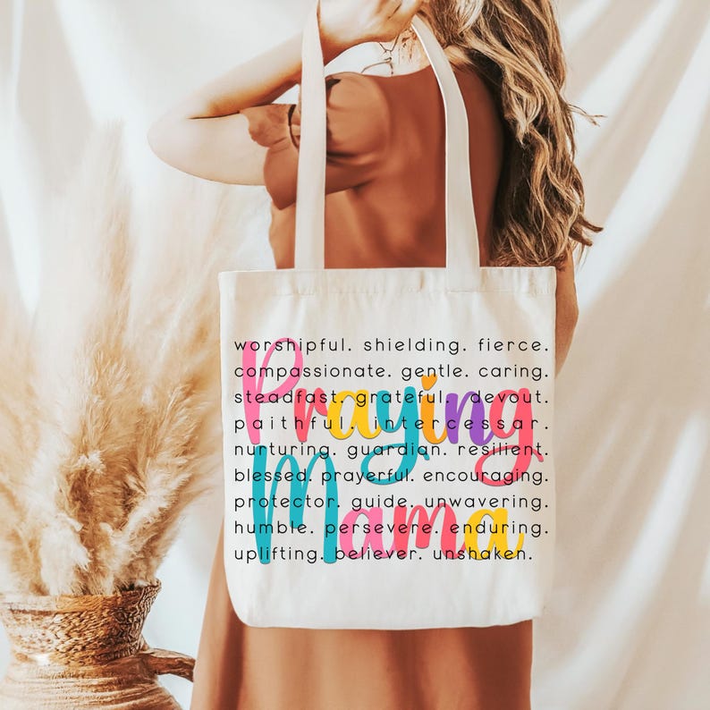 Peut inclure: Un sac fourre-tout en toile blanche avec le mot "Prier" en lettres color&eacute;es et une liste de mots d&eacute;crivant les qualit&eacute;s d'une personne qui prie. Les mots incluent : respectueux, protecteur, f&eacute;roce, compatissant, doux, attentionn&eacute;, ferme, reconnaissant, d&eacute;vou&eacute;, fid&egrave;le, intercesseur, nourricier, gardien, r&eacute;silient, b&eacute;ni, fervent, encourageant, protecteur, guide, in&eacute;branlable, humble, pers&eacute;v&eacute;rant, durable, &eacute;difiant, croyant, in&eacute;branlable.