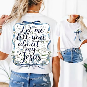 Pode incluir: Camiseta branca com a frase "Let me tell you about my Jesus" em um design floral azul. O design inclui fitas e flores azuis. Uma versão menor do design está na área do bolso frontal.
