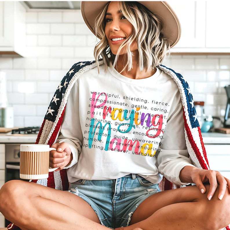 Peut inclure: Un t-shirt blanc &agrave; manches longues avec le mot "Mama" &eacute;crit en lettres color&eacute;es. Le t-shirt comporte une description textuelle du mot "Mama" avec des attributs positifs tels que "respectueux", "fier", "compassionn&eacute;", "ferme", "intercesseur", "gardien", "r&eacute;silient", "priant", "protecteur", "guide", "in&eacute;branlable", "pers&eacute;v&eacute;rant", "endurant", "croyant" et "in&eacute;branlable".