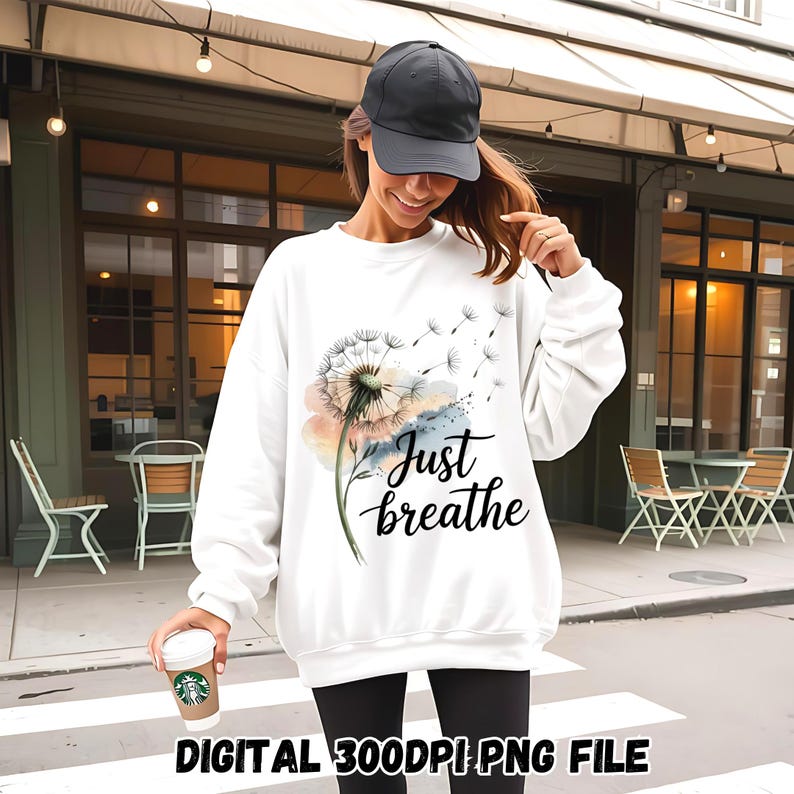 K&ouml;nnte beinhalten: Wei&szlig;er Pullover mit einem Aquarell-L&ouml;wenzahnmuster und dem Text "Just breathe".