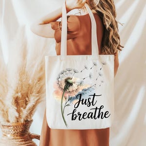 K&ouml;nnte beinhalten: Wei&szlig;e Stofftasche mit einem Aquarell-L&ouml;wenzahnmuster und dem Text "Just breathe".