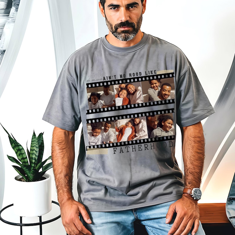 Pu&ograve; includere: T-shirt grigio con un design a striscia di pellicola che mostra foto di famiglia e la scritta "AIN'T NO HOOD LIKE FATHERHOOD". La maglietta ha una vestibilit&agrave; ampia e maniche corte. La data "05.08.2023" &egrave; stampata sopra.