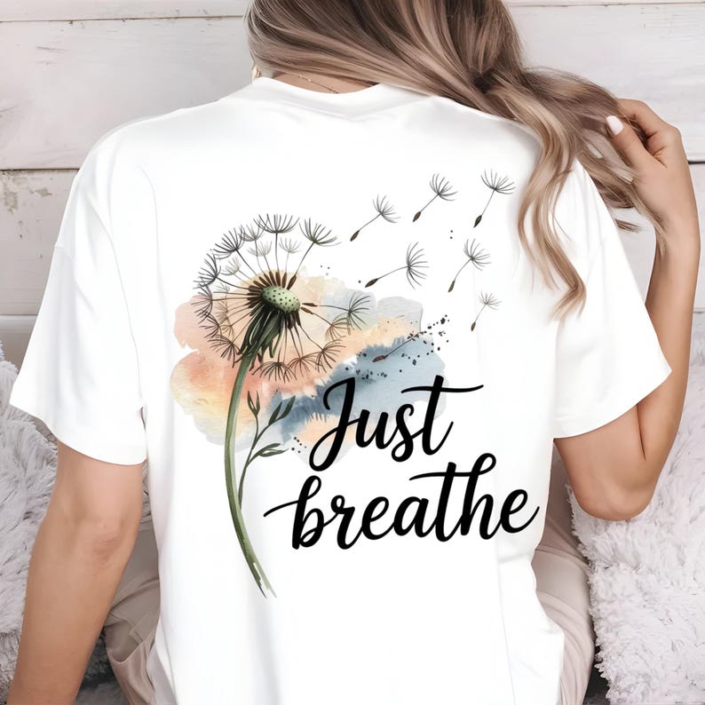 K&ouml;nnte beinhalten: Wei&szlig;es T-Shirt mit einem Aquarell-L&ouml;wenzahnmuster und dem Text "Just breathe" auf der R&uuml;ckseite.