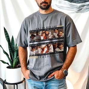 Pu&ograve; includere: T-shirt grigio con un design a striscia di pellicola che mostra foto di famiglia. Il testo sulla maglietta recita "AIN'T NO HOOD LIKE FATHERHOOD". La maglietta ha una vestibilit&agrave; ampia e maniche corte.