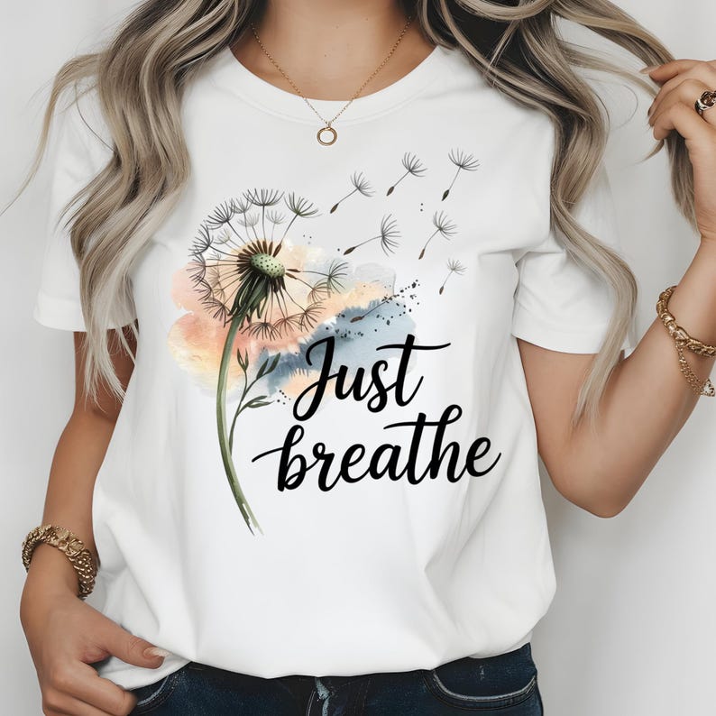 K&ouml;nnte beinhalten: Wei&szlig;es T-Shirt mit einem Aquarell-L&ouml;wenzahnmuster und dem Text "Just breathe" in Schwarz.