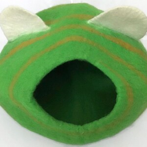 Puede incluir: Cama para mascotas de fieltro verde con dos orejas de fieltro blanco. La cama tiene un patrón de rayas con rayas marrones.