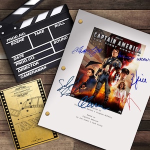 以下が含まれることがあります： 映画をテーマにしたディスプレイ。映画の小道具である、撮影用ボード、俳優のサインが入った「キャプテン・アメリカ/ザ・ファースト・アベンジャー」の脚本、サインキーが写っています。脚本の表紙にはキャプテン・アメリカが描かれています。木製の表面に配置されています。