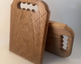 May include: Two wooden cutting boards with carved diamond patterns and handle cutouts. The boards are a warm brown color and appear to be made of hardwood. The handles have a unique, three-hole design.