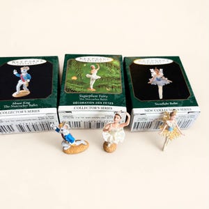 Puede incluir: Tres figuras en miniatura de la serie Collector's Series de Hallmark Keepsake Ornament, que incluyen un Rey Ratón, un Hada de Azúcar y una bailarina del Ballet de Copos de Nieve, cada una frente a su caja de cartón verde oscuro.