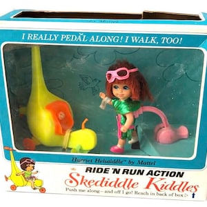 May include: A vintage Skediddle Kiddles toy set in its original box. The box features a clear window showcasing a doll with pink goggles and a green outfit, along with a yellow vehicle. Text on the box reads "Ride 'N Run Action".