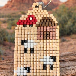 May include: Handmade beaded earrings in a geometric design. The earrings feature a tan background with black, white, red, and brown accents. The earrings are rectangular with a curved top and a silver-tone ear wire.