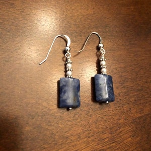 May include: A pair of silver earrings with blue and white gemstone drops. The earrings have a silver hook and are decorated with small silver beads.