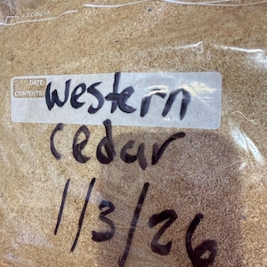 Könnte beinhalten: Ein klarer Plastikbeutel gefüllt mit hellbraunen Holzspänen. Ein weißes Etikett auf dem Beutel trägt die Aufschrift "western cedar" und das Datum "1/3/26" mit schwarzem Marker.