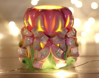 May include: A pink and green carved candle with a floral design. The candle is lit and the flame is visible.