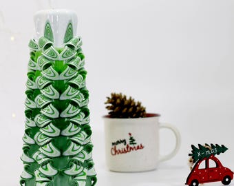 May include: A green and white Christmas tree candle with a white top. The candle is decorated with a swirling pattern and is shaped like a Christmas tree.