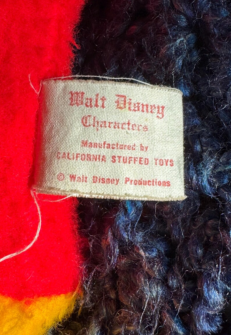 Op de afbeelding: Een wit label met zwarte tekst dat "Walt Disney Characters Manufactured by California Stuffed Toys &copy; Walt Disney Productions" zegt.