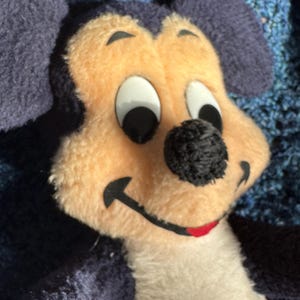 Op de afbeelding: Een pluche Mickey Mouse speelgoed met zwarte oren, een zwarte neus en witte ogen. Het speelgoed draagt een rood-witte outfit.