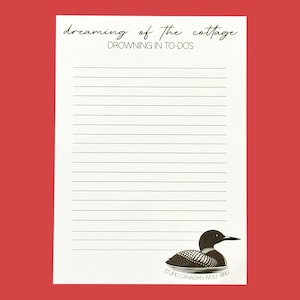 Puede incluir: Bloc de notas rayado con el texto "dreaming of the cottage" y "drowning in to-dos" en fuente cursiva. Una ilustración en blanco y negro de un somorgujo en la parte inferior, con el texto "STUPID CANADIAN WOLF BIRD". El fondo es rojo.