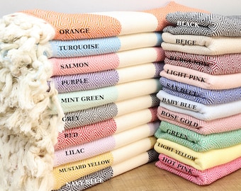 May include: A stack of colorful Turkish towels with diamond patterns and fringed edges. The towels come in various colors, including orange, turquoise, salmon, purple, mint green, grey, red, lilac, mustard yellow, black, beige, burgundy, light pink, sax blue, baby blue, rose gold, green, light yellow, and hot pink.