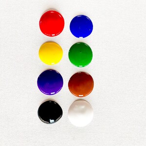 以下が含まれることがあります： ふた付きの丸い絵の具の容器が8つ、4つずつ2列に並んでいます。色は赤、青、黄、緑、紫、茶色、黒、白です。