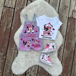 May include: A set featuring pink and blue denim overalls with Minnie Mouse graphics and the name Journee, a white t-shirt with the text Oh Twodles and Birthday Girl Journee, and two white high-top sneakers with pink laces and Minnie Mouse designs.