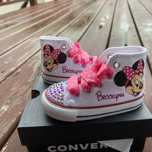 May include: White high-top sneakers with pink polka dot ribbon laces and a Minnie Mouse design. The sneakers are decorated with rhinestones and the name "Brooklynn" is written on the side.
